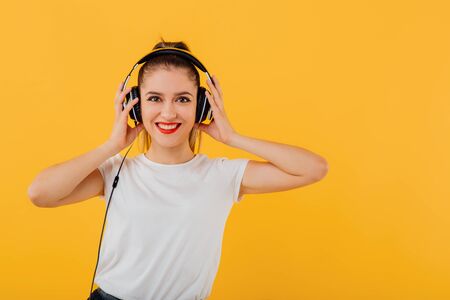 happy teenager smiles with headphones on head, looking at camera dressed in a white shirt, positive emotional state  isolated on a yellow backgroundの写真素材