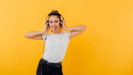 happy and distracted girl with headphones, dressed in a white shirt, positive emotional state  isolated on a yellow backgroundの写真素材