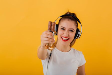 beautiful girl happy and smiling with headphones on head looks at camera is chocolate bar in hand dressed in a white shirt, positive emotional state  isolated on a yellow background, copy spaceの写真素材