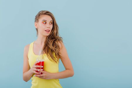 beautiful girl smiles amazed, has the drink bottle in his hand and looks sideways, positive facial emotions, isolated on blue background, copy spaceの写真素材