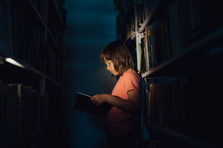 the little girl reads from the book, learns in the old library, profile view, indoorsの写真素材