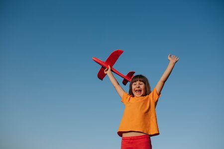 happy little girl playing with a toy airplane outdoor, dreams of flying, outdoors, sky background, copy spaceの写真素材