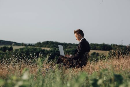 blogger using laptop in the field, sat down in suit, profile view, outdoorの写真素材