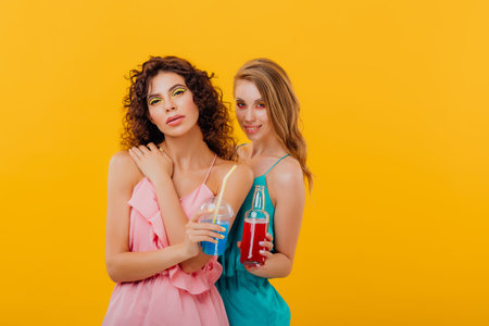 two beautiful girls with a bottle of drink in the hand and a plastic cup with juice, positive facial...