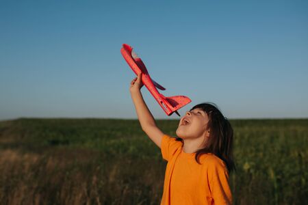 A cheerful little  girl playing with a toy airplane outdoor, dreams of traveling, outdoors, sky backgroundの写真素材