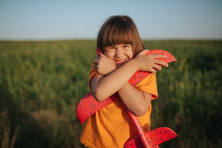 girl is holding red plane, dressed in orange shirt, look at the camera, outdoorsの写真素材