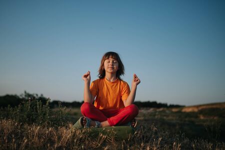 Happy little girl meditates, yoga, dressed in orange shirt, outdoorsの写真素材