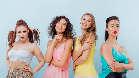 four happy young girls with hairstyle and unusual makeup, look at the camera, isolated blue background, positive facial emotions, copy spaceの写真素材