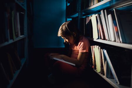 little girl reads a book, she is surprised. learns in the library, sitting down, profile view, indoors,の写真素材
