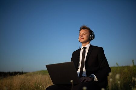 young happy man with headphones listening music in field, laptop outdoorの写真素材