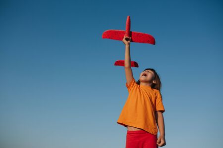 A cheerful little  girl playing with a toy airplane outdoor, dreams of flying, outdoors, sky background, copy spaceの写真素材