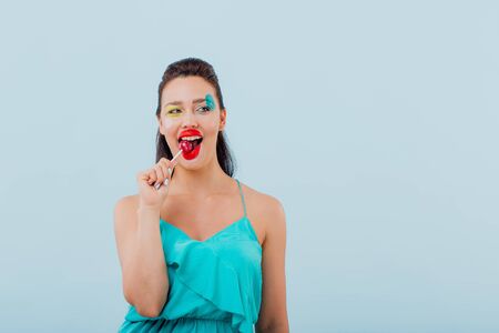 young girl has chupa chups in mouth, hairstyle and makeup unusual, isolated blue background, positive facial emotions, copy spaceの写真素材