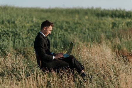 excited businessman sitting on the chair with laptop and smiling, profile view, outdoorの写真素材