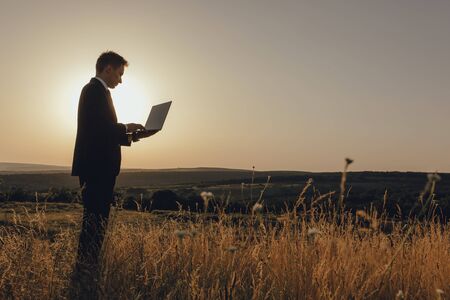 young man using laptop, Internet and social network concept, at sunset, copy space, profile view, outdoorの写真素材