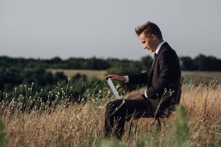 young businessman with laptop in the field, outdoor, profile viewの写真素材