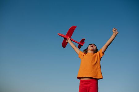 emotionally little girl playing with a toy airplane outdoor, dreams of flying, outdoors, sky background, copy spaceの写真素材