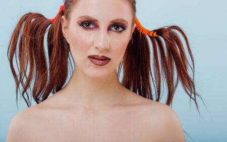 close up. young girl hairstyle and makeup unusual is holding two plastic cups juice, look at the camera, isolated blue background, positive facial emotions, copy spaceの写真素材