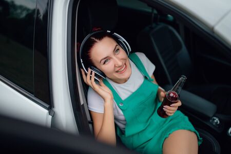teen with headphones on head. smiles is happy, has the drink bottle in his hand. sitting in the car.  outdoorの写真素材