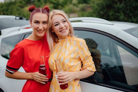two beautiful young women, having fun in red and yellow dresses, has the drink bottle in his hand. next to the car, outdoorの写真素材
