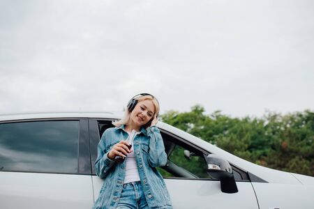portrait of a happy teenager. with headphones. listen to music, have drink bottle in hand. copy space, Besides car,  outdoorの写真素材