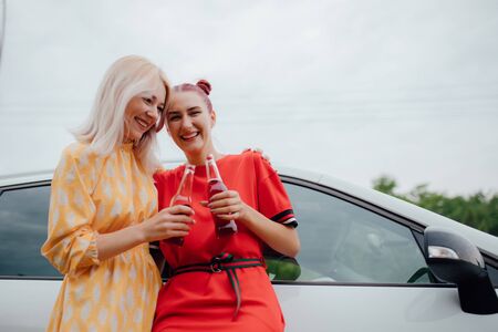 two girlfriends are cheerful, having fun in red and yellow dresses, has the drink bottle in his hand. next to the car, outdoorの写真素材