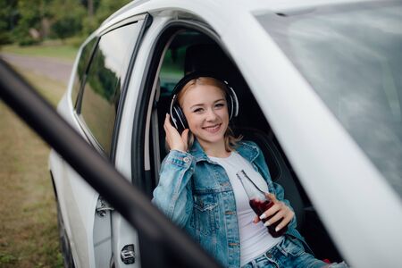 happy teenager with headphones. looks at the camera, has the drink bottle in his hand. sitting in the car. outdoorの写真素材