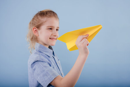 happy child girl holds yellow paper plane in his hand,