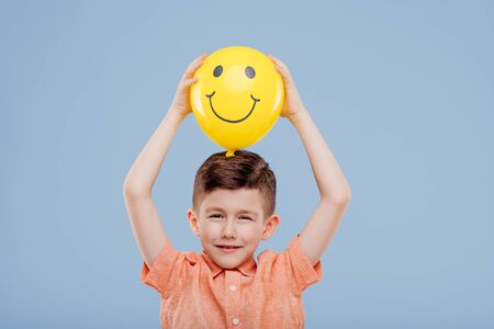 little boy holds up yellow balloon with smile.の写真素材