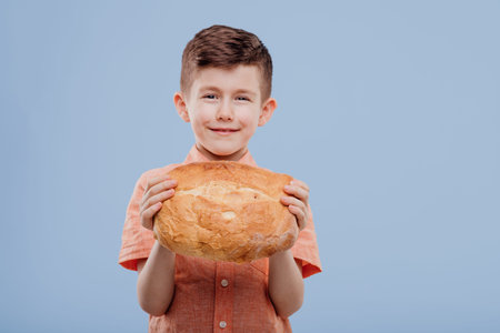 kid little boy holding a bread, looks at the camera, isolated on blue background,の写真素材
