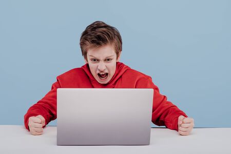 Angry schoolboy using laptop in studioの写真素材