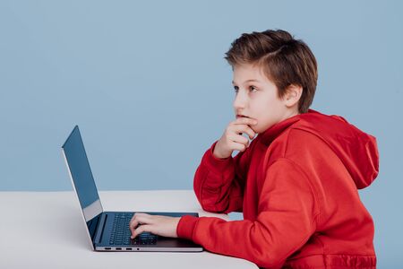 Thinking boy looks to the side, near the laptopの写真素材