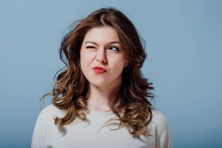 girl makes grimaces, looking away against blue backgroundの写真素材