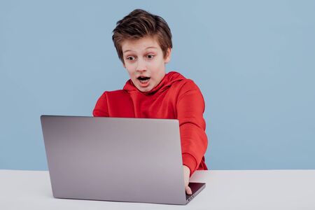 Excited boy using laptop in studio blue backgroundの写真素材