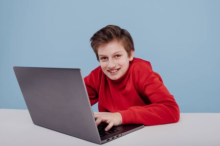 boy near the table with laptop blue backgroundの写真素材