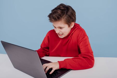 Irritated child boy in red sweatshirt typing on laptopの写真素材