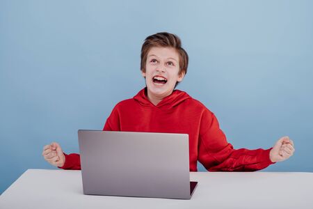 screaming. angry child boy in red sweatshirt. near laptopの写真素材