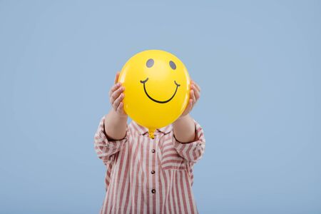 little child girl covering face with yellow balloon with smile,の写真素材