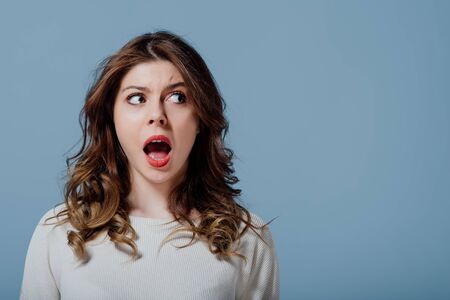 Puzzled young woman with open mouth blue backgroundの写真素材