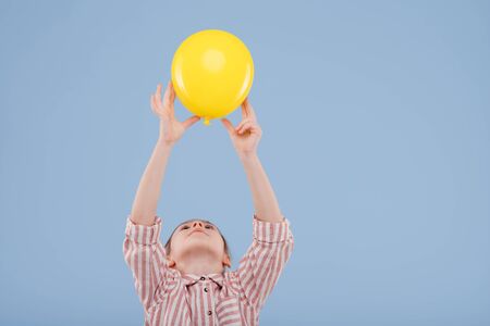 child girl holds up yellow balloon. dressed in striped shirt,の写真素材