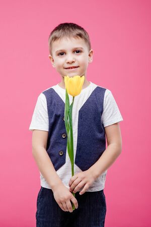 portrait of smiling little boy holding a yellow tulip floweの写真素材