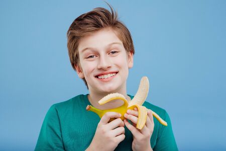 smiling young boy with a banana in his handin green t-shirtの写真素材