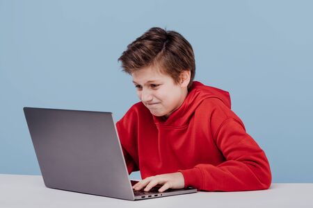 Nervous child boy in red sweatshirt typing on laptopの写真素材