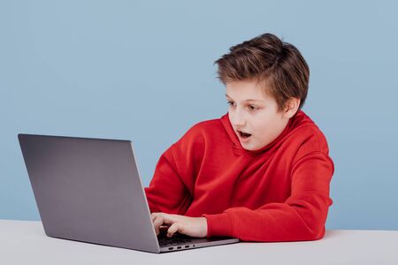 excited boy in red sweatshirt playing on laptopの写真素材