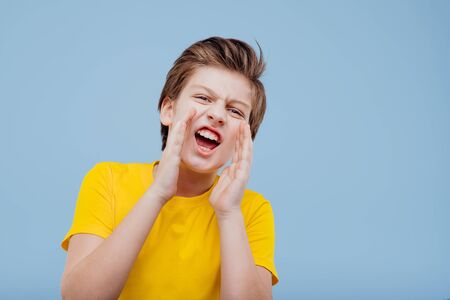enervant preteen boy looks at camera and screaming in yellow t-shirt isolated on yellow background, copy spaceの写真素材