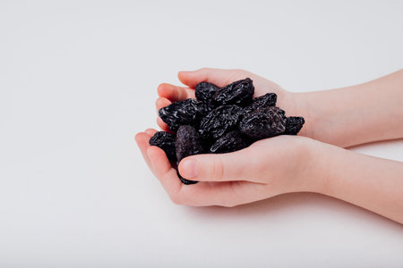 Prune dry. child hand holding dried plum resting isolated on white background, close up