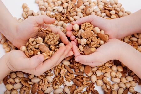 close up, four hands of a child with assortment of nuts. walnut, pistachio, almonds, hazelnuts, on white background, top viewの写真素材