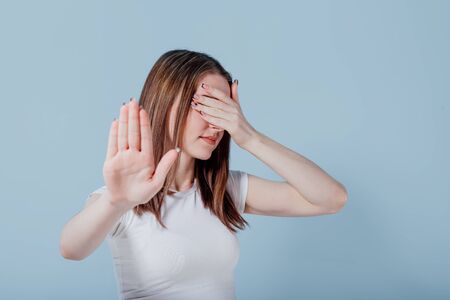 Beautiful brunette young woman hiding, covered eyes with hand palm isolated over blue wall background, studio portrait. People lifestyle fashion concept. Mock up copy spaceの写真素材