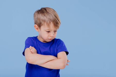 angry child llittle boy dressed in blue T-shirt, isolated on blue background, in studioの写真素材