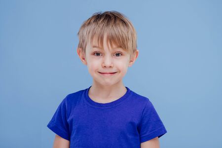 nice smiling little boy looks at the camera dressed in blue T-shirt, isolated on blue background, in studioの写真素材
