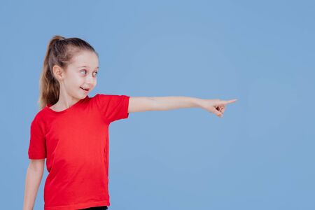 Confident positive little girl in casual outfit and pointing away while standing in studio against blue backgroundの写真素材